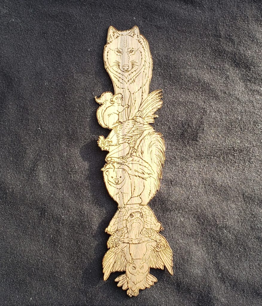 A photo of a wooden bookmark with a wolf, squirrel, rooster, cockroach, skunk, turtle, and owl engraved into the wood with their forms cut out.